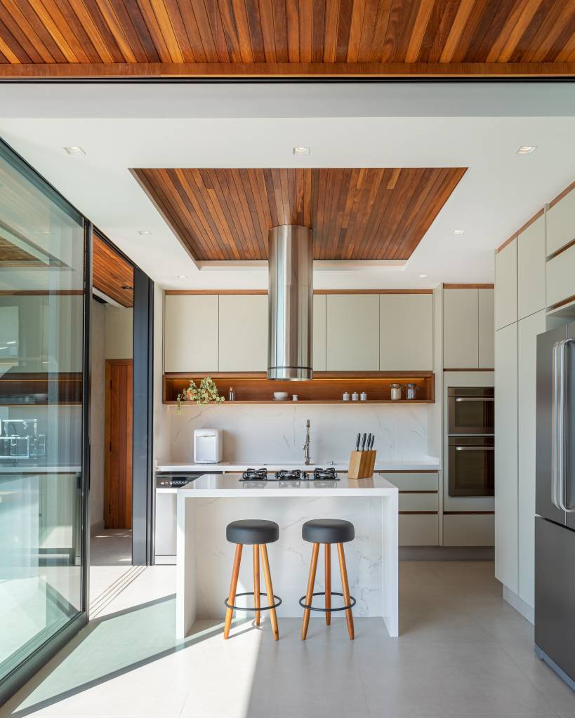 Casa de praia com varanda tem forro e painel ripado para criar estética elegante. Projeto de Ana Gadioli Arquitetura. Na foto, cozinha branca minimalista.