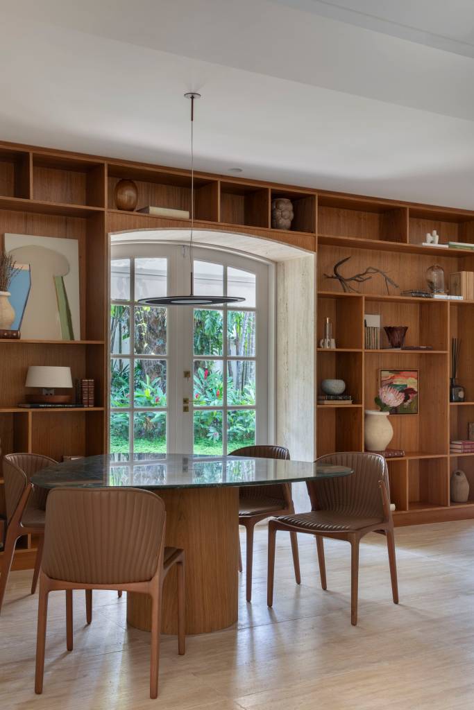Casa em estilo clássico europeu tem piso mármore e árvore na área gourmet. Projeto de Studio LAK. Na foto, mesa, estante de nichos.