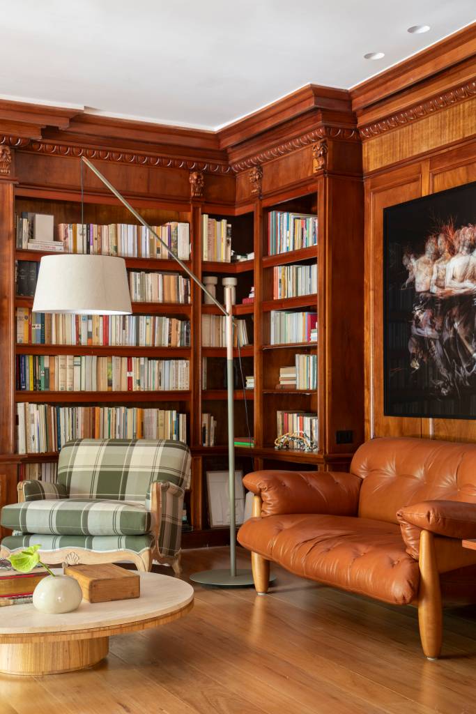Casa em estilo clássico europeu tem piso mármore e árvore na área gourmet. Projeto de Studio LAK. Na foto, escritório, estante de livros, poltronas.