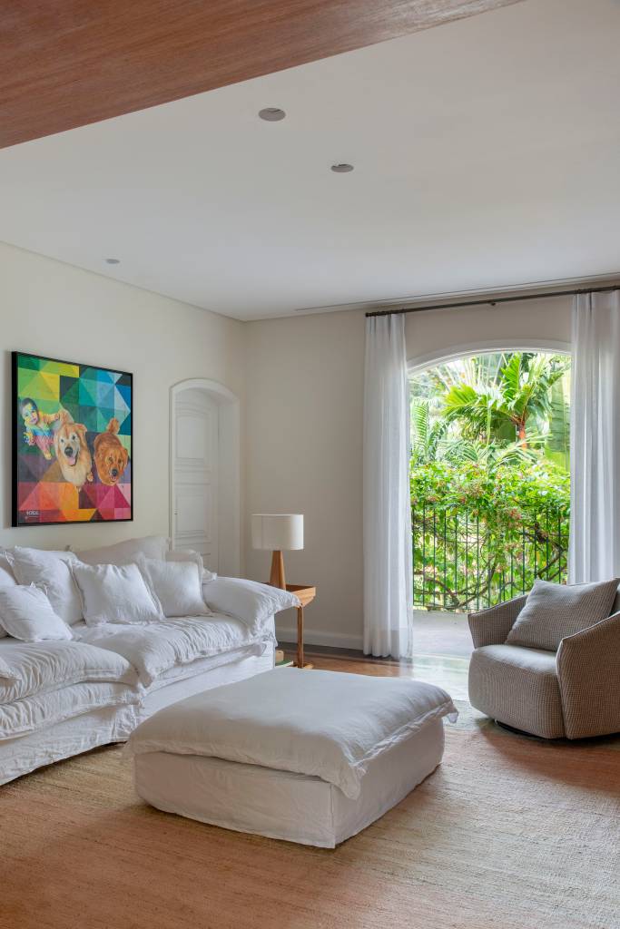 Casa em estilo clássico europeu tem piso mármore e árvore na área gourmet. Projeto de Studio LAK. Na foto, sala, sofá branco, pufe, poltrona, cortina.