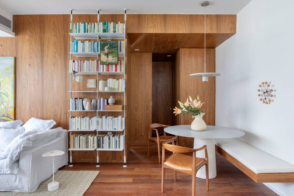 Cozinha de ape de 80 m² é minimalista com laca branca na marcenaria. Projeto de João Panaggio. Na foto, sala de jantar, mesa redonda, estante de livros.
