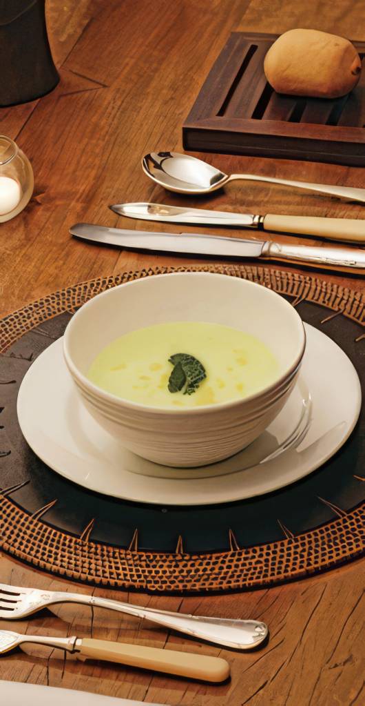 A imagem apresenta um creme frio de melão servido em um bowl decorado com folhas de hortelã fresca e raspas de limão, destacando a textura suave e a cor vibrante do melão, tornando-o um prato atrativo e refrescante para o verão.