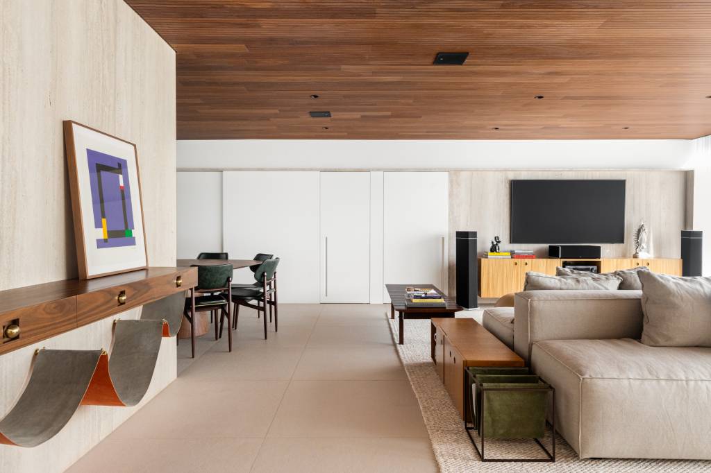 Forro de madeira e painel de mármore são destaques em área social de apartamento. Sala de estar e jantar.