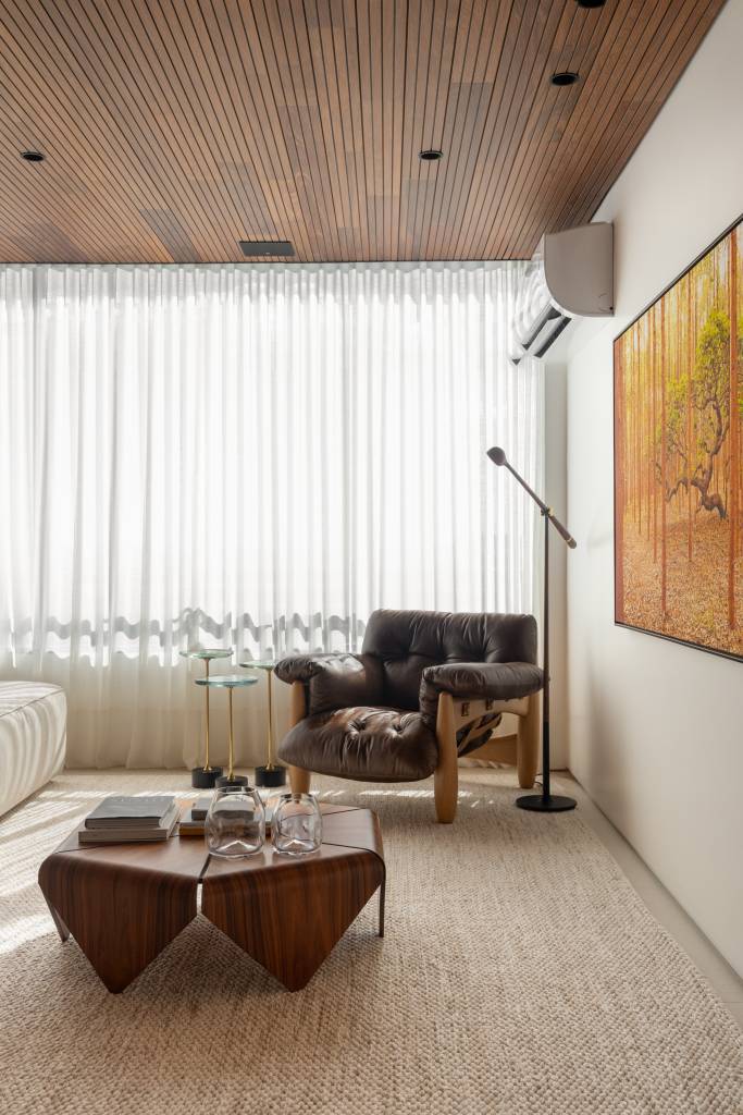 Forro de madeira e painel de mármore são destaques em área social de apartamento. Sala de estar.