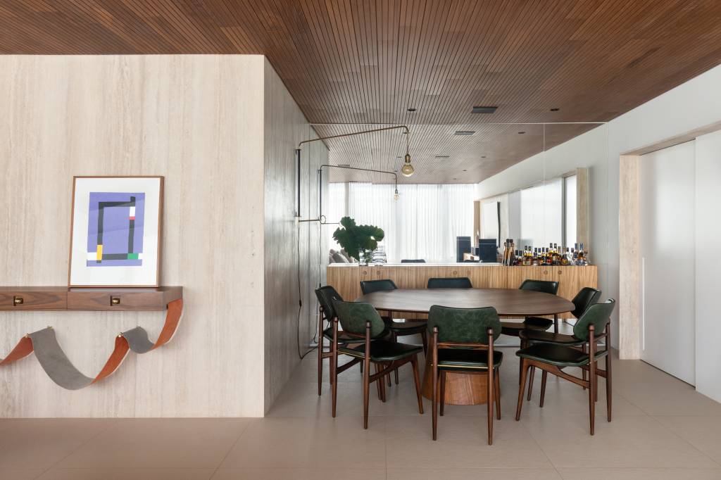 Forro de madeira e painel de mármore são destaques em área social de apartamento. Sala de jantar.
