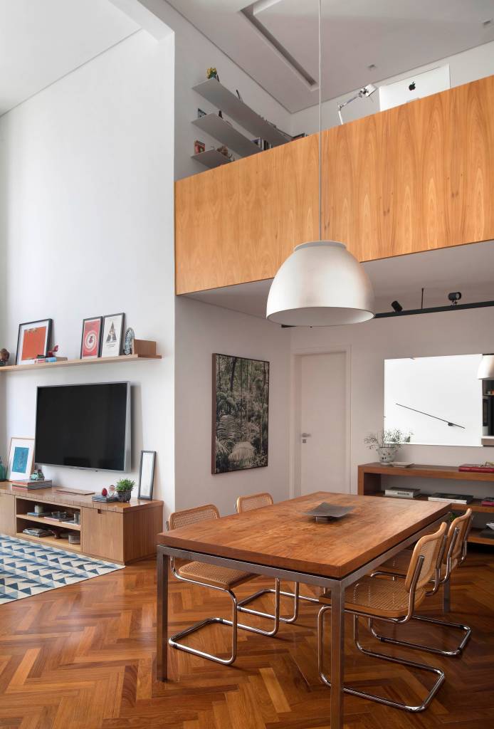 Reforma em apê cria mezanino na sala a partir de estrutura metálica. Projeto de Carolina Gouvea. Na foto, sala de jantar, sala de estar, cadeiras com encosto de palhinha.