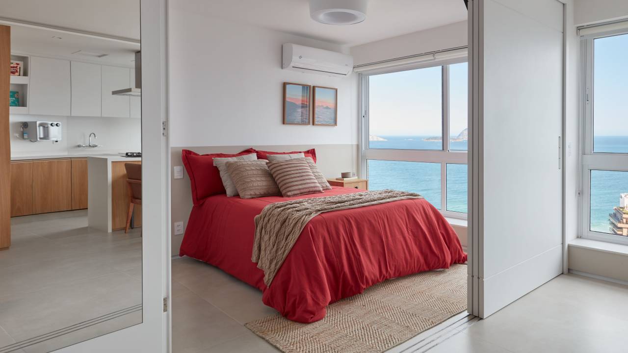 Apê de 50 m² tem portas de correr e bancada de trabalho na estante. Projeto de Carolina Gouvea Arquitetura. Na foto, quarto, roupa de cama vermelha.