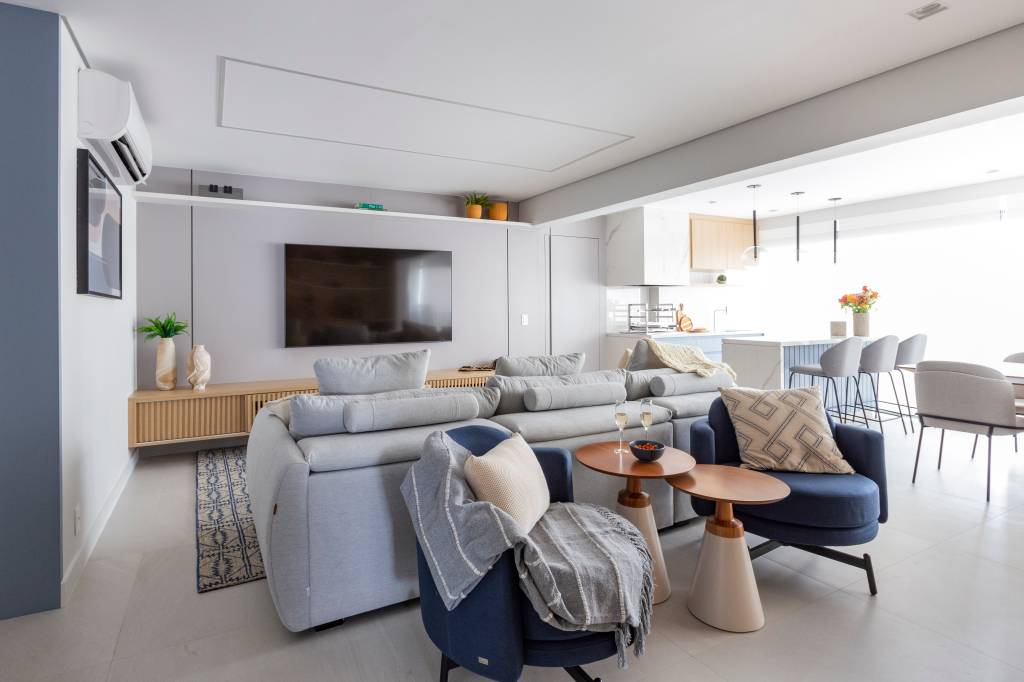 Azul é protagonista em apê com varanda integrada e área gourmet. Projeto de Mari Milani, sala, sofá cinza, poltronas.