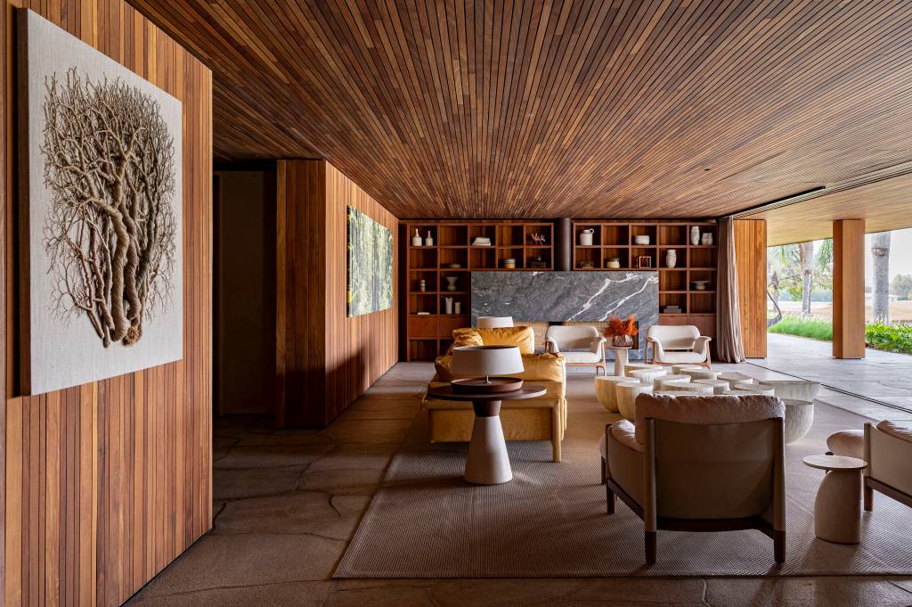 Casa de campo tem piscina semiolímpica e oito suítes elegantes. Projeto de Studio DWG. Na foto, sala de estar, painéis de madeira nas paredes e teto.