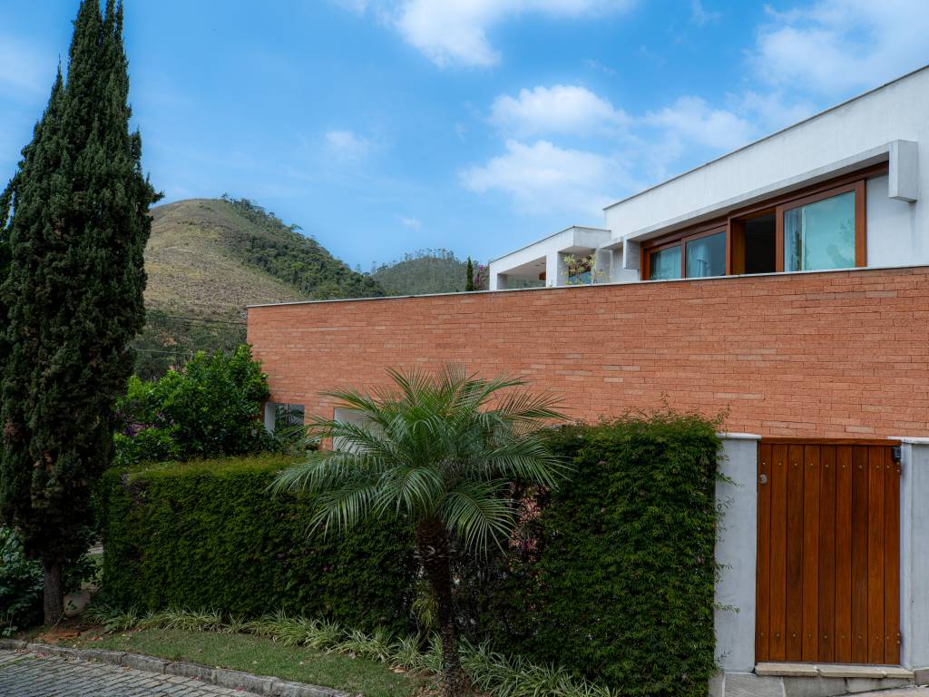 Casa em Teresópolis tem esquadrias, tijolinhos e cimento queimado na fachada. Projeto de Viviane Cunha.