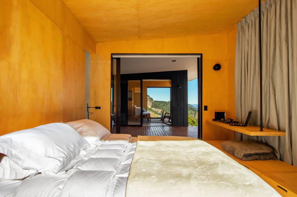 Chalé de apenas 48 m² tem paredes com painéis de madeira e vista para serra. Projeto de RAWI Arquitetura+Design. Na foto, quarto, cama de casal.