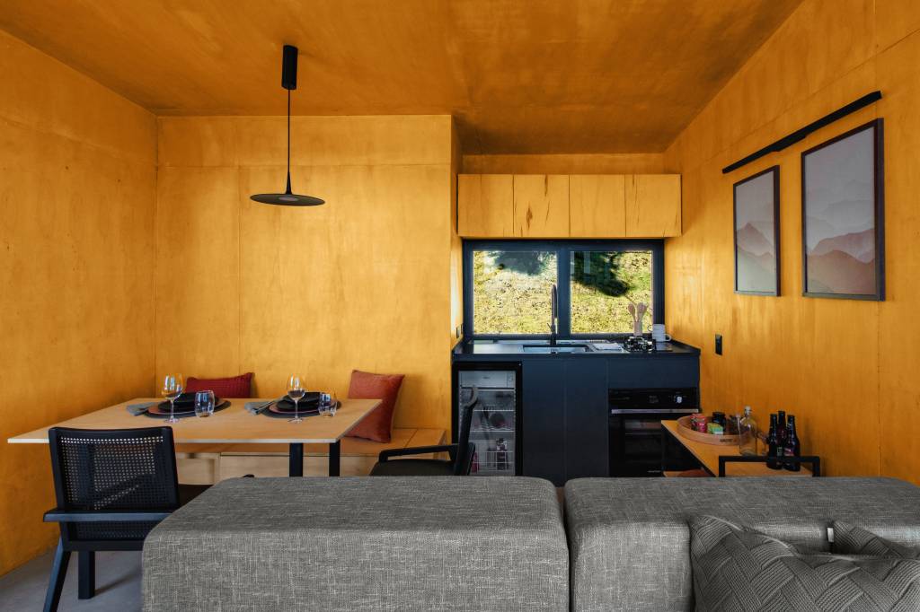 Chalé de apenas 48 m² tem paredes com painéis de madeira e vista para serra. Projeto de RAWI Arquitetura+Design. Na foto, sala com cozinha integrada.