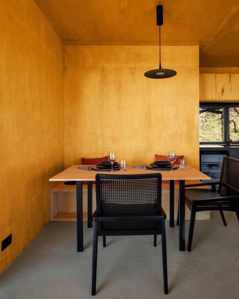 Chalé de apenas 48 m² tem paredes com painéis de madeira e vista para serra. Projeto de RAWI Arquitetura+Design. Na foto, sala de jantar pequena, cadeiras pretas.