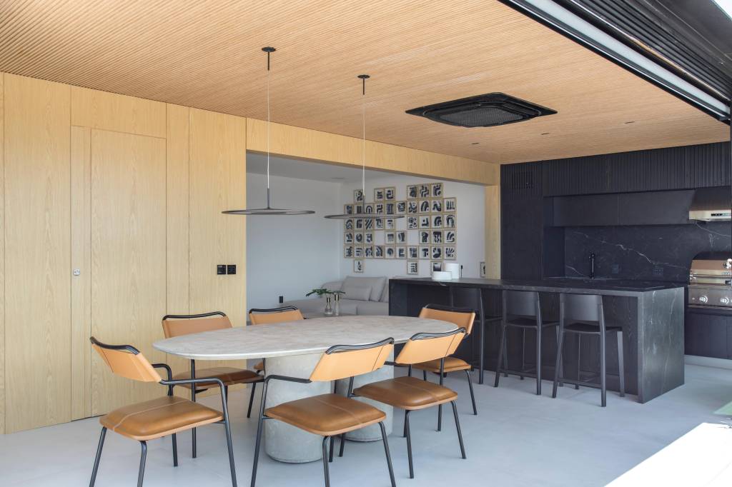 Cobertura elegante tem piso de porcelanato e escada com degraus em Dekton. Projeto BF+Arquitetos. Na foto, sala de jantar, mesa oval, área gourmet com revestimentos pretos.