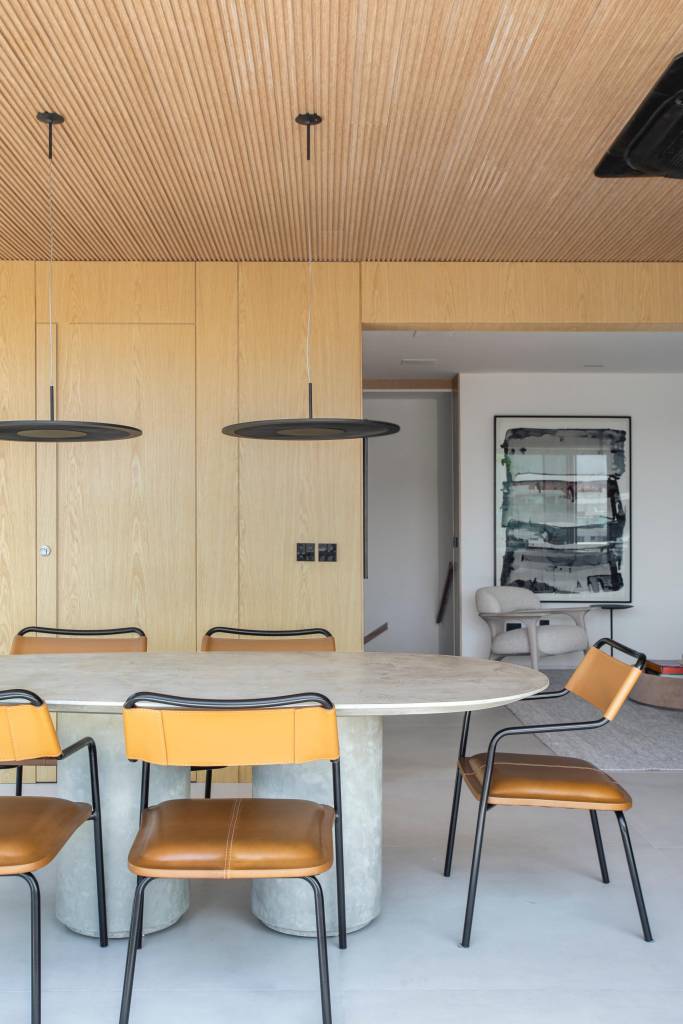 Cobertura elegante tem piso de porcelanato e escada com degraus em Dekton. Projeto BF+Arquitetos. Na foto, sala de jantar, mesa oval, painéis de madeira.