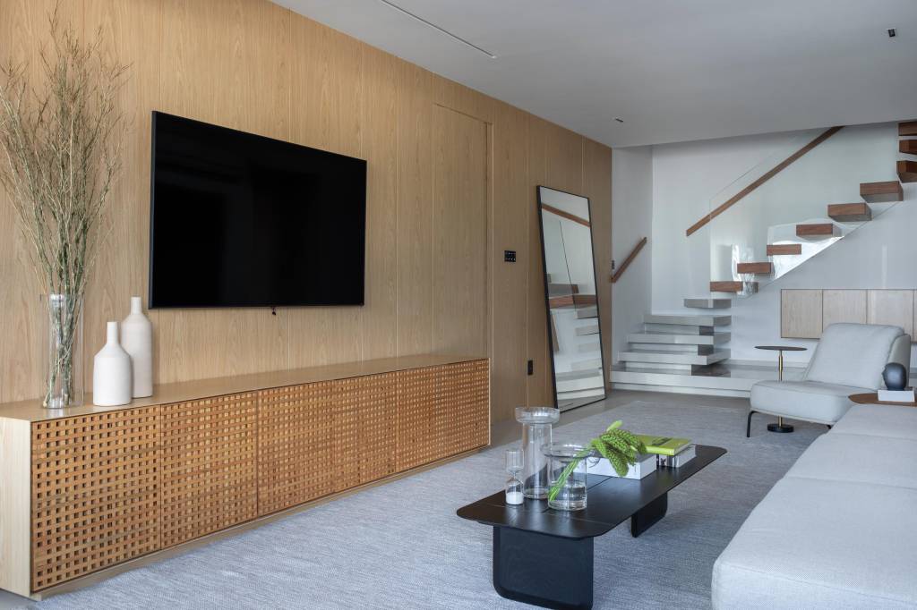 Cobertura elegante tem piso de porcelanato e escada com degraus em Dekton. Projeto BF+Arquitetos. Na foto, sala de estar, painéis de madeira na parede.
