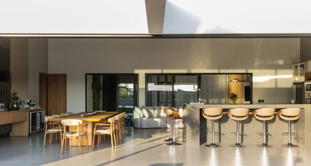 Residência de 847 m² tem projeto contemporâneo voltado ao conforto e à convivencia. Projeto de Natália Sundfeld. Na foto: casa em estilo contemporâneo, churrasqueira, bancada, banquetas altas, mesa de jantar, cadeiras, estofado