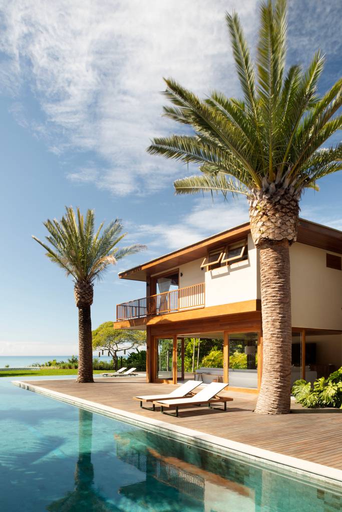 Teto de casa de praia tem forro em madeira cumaru com palha de dendê trançada. Projeto de David Bastos. Na foto, fachada, palmeiras, piscina.