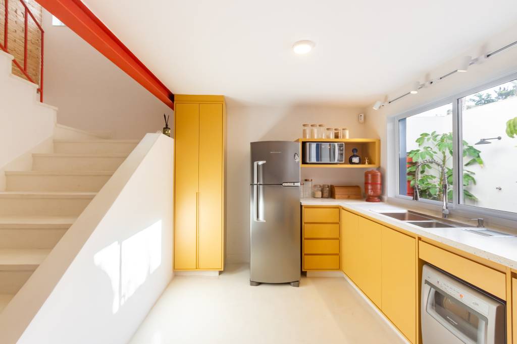 Casa com parede de tijolinhos e detalhes em cores primárias. Projeto de Sertão Arquitetos. Na foto, cozinha com armários em amarelo.