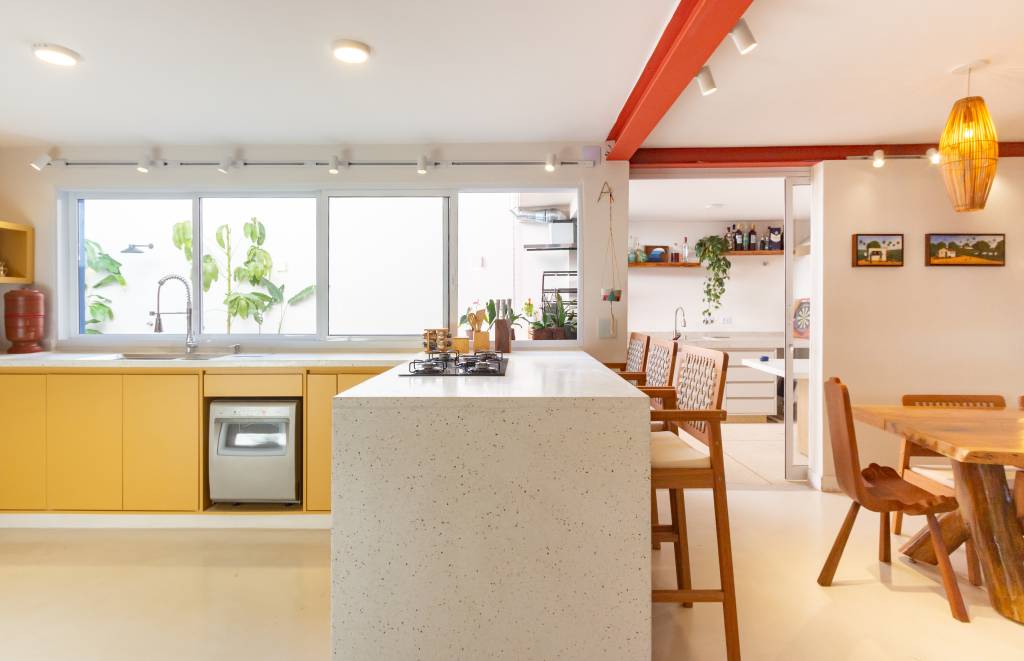 Casa com parede de tijolinhos e detalhes em cores primárias. Projeto de Sertão Arquitetos. Na foto, cozinha com balcão e banquetas.