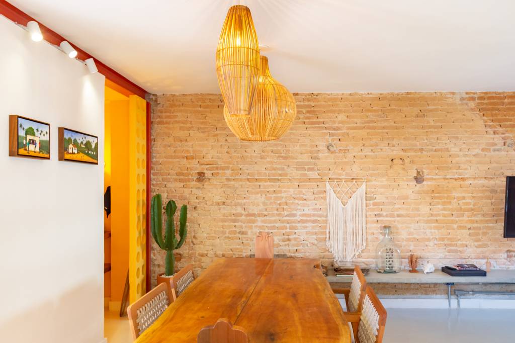 Casa com parede de tijolinhos e detalhes em cores primárias. Projeto de Sertão Arquitetos. Na foto, uma mesa de jantar com luminária suspensa acima.