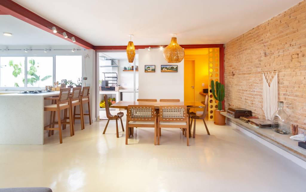 Casa com parede de tijolinhos e detalhes em cores primárias. Projeto de Sertão Arquitetos. Na foto, cozinha, sala de estar e jantar integradas.
