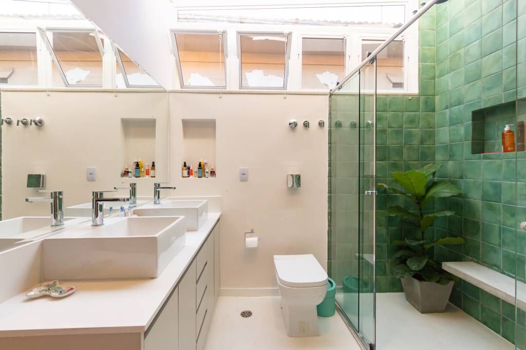 Casa com parede de tijolinhos e detalhes em cores primárias. Projeto de Sertão Arquitetos. Na foto, banheiro grande com vaso de planta dentro do box.