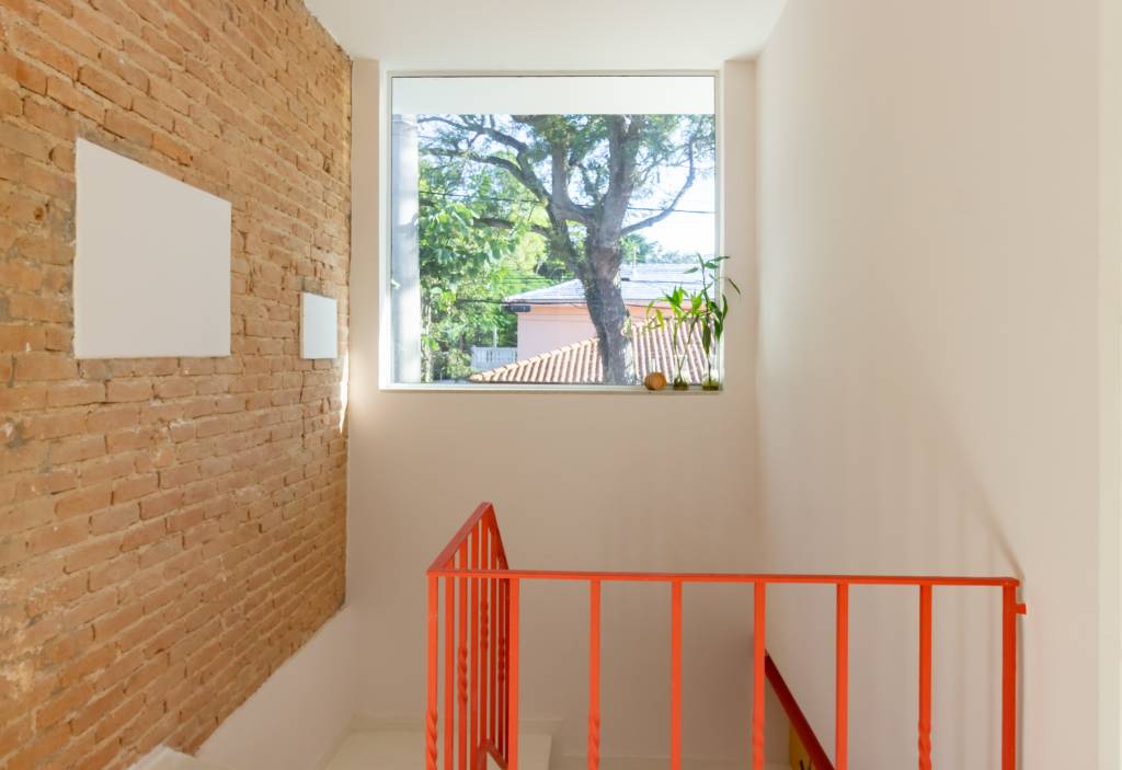 Casa com parede de tijolinhos e detalhes em cores primárias. Projeto de Sertão Arquitetos. Na foto, escada com detalhes em vermelho.