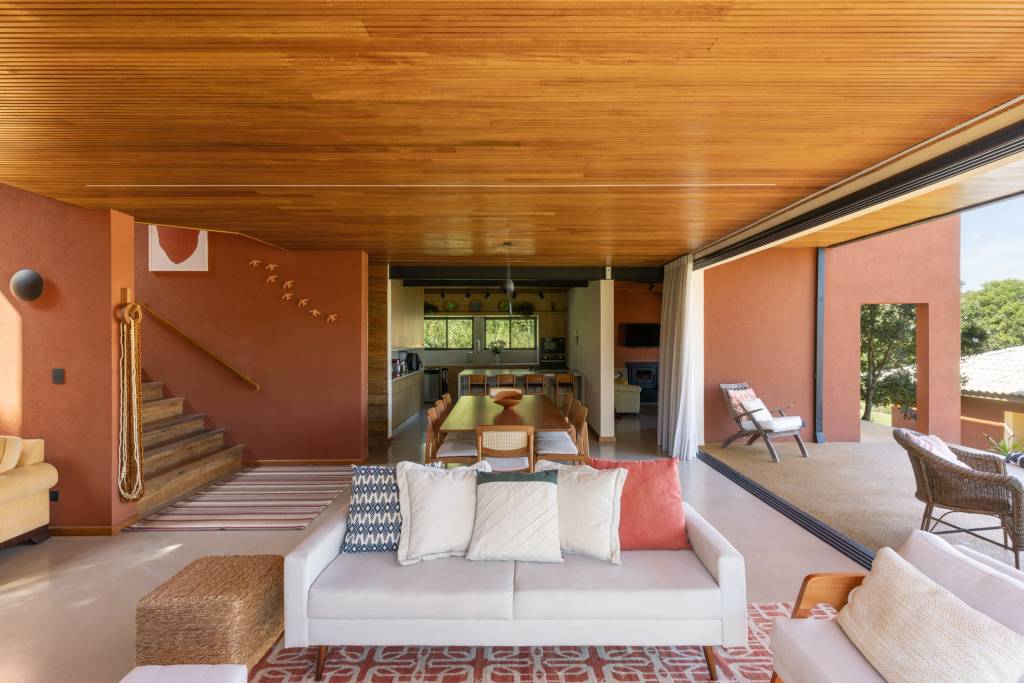 Casa nos arredores de São Paulo tem tons de terracota no interior e exterior. Projeto de Sertão Arquitetos. Na foto, sala extensa com sofá branco.