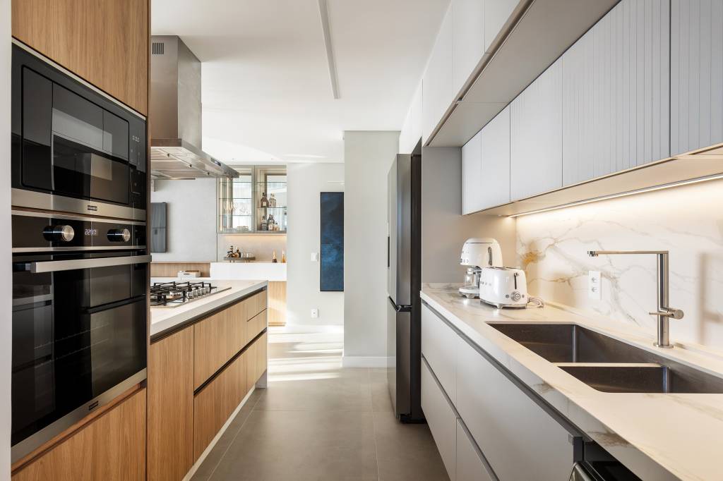 Design minimalista: apê em Jurerê Internacional une funcionalidade e elegância. Projeto de Jeane Silva. Na foto, cozinha armários em tom amadeirado e branco.