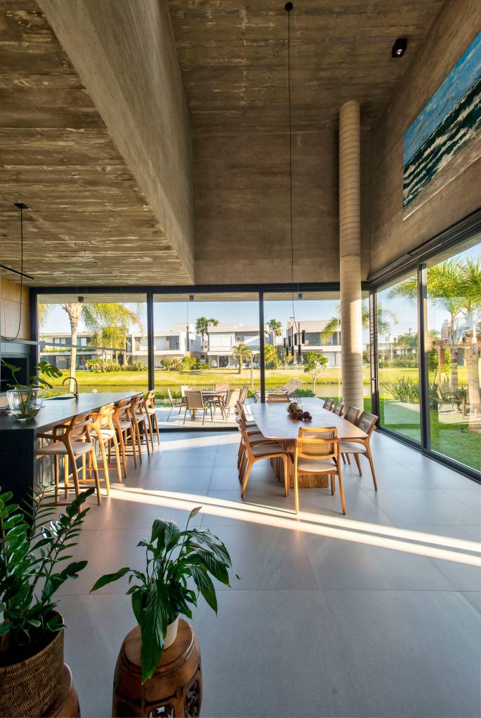 Casa de praia de 406 m² combina brutalismo, arte e sustentabilidade. Projeto de Mayresse Arquitetura. Na foto, sala de estar com janelas de vidro.