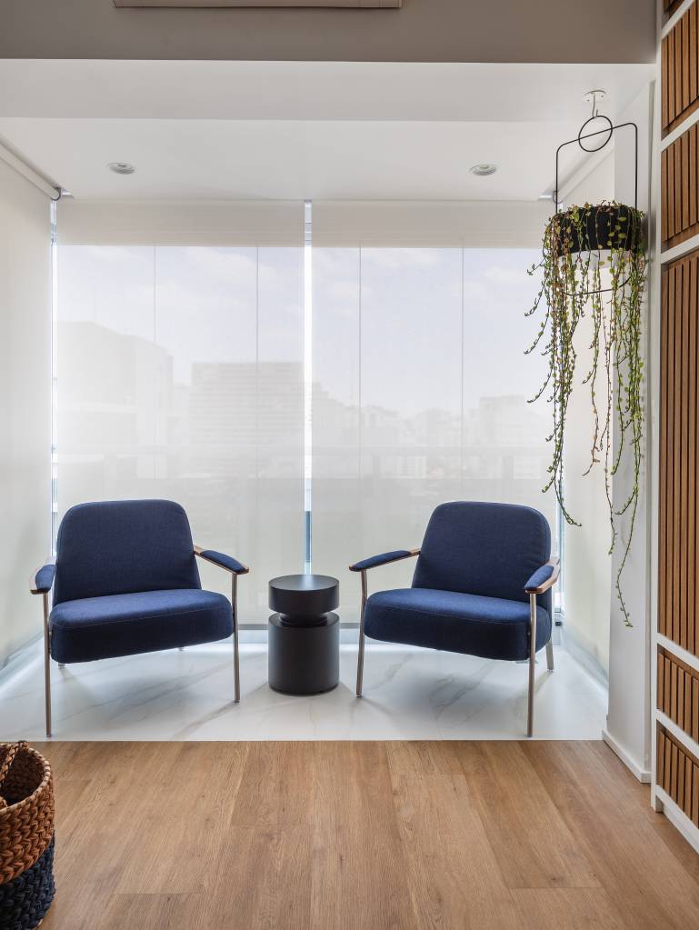 Apartamento compacto de 38 m² tem piso vinílico aquecido e canto alemão. Na foto, varanda, poltronas azuis.