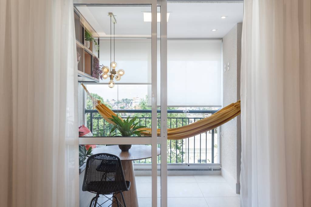 Varanda de apartamento tem serralheria preta com nichos e rede amarela. Projeto de RMV Interiores.