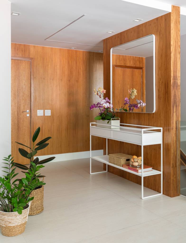 Apê tem estante tipo colmeia que abriga 15 nichos e cristaleira. Projeto de Ikeda Arquitetura. Na foto, entrada de apartamento com aparador.