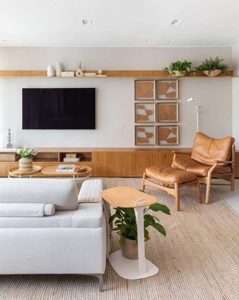 Apê tem estante tipo colmeia que abriga 15 nichos e cristaleira. Projeto de Ikeda Arquitetura. Na foto, sala com poltrona em couro.