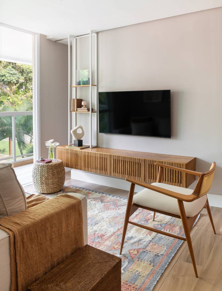 Apê tem estante tipo colmeia que abriga 15 nichos e cristaleira. Projeto de Ikeda Arquitetura. Na foto, sala de TV com rack de madeira.