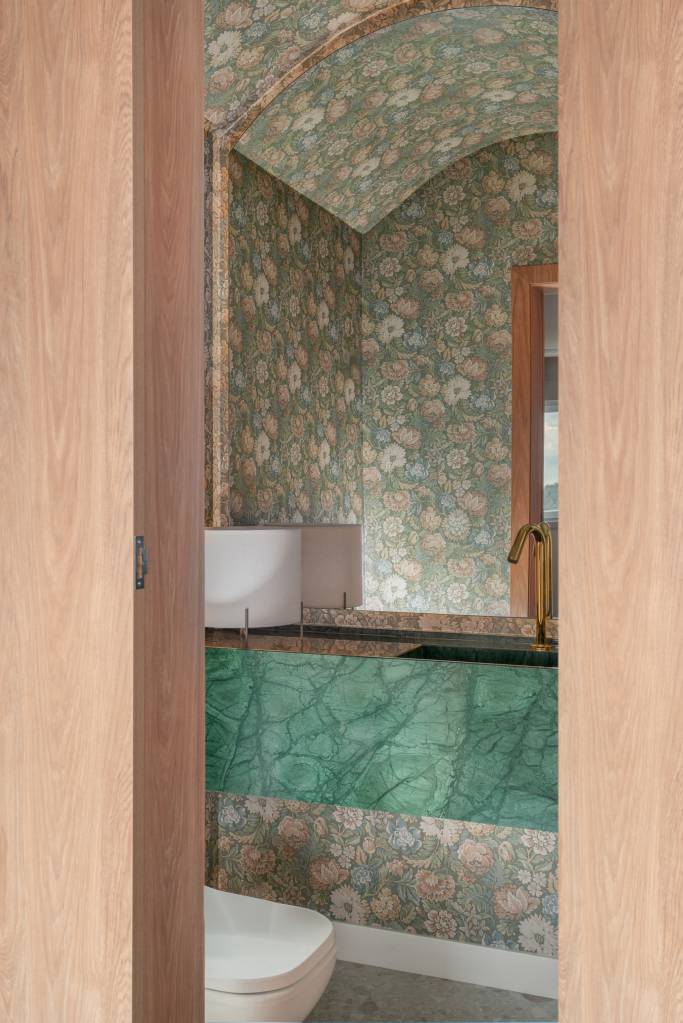 Lareira em mármore verde se destaca em apartamento de 170 m². Projeto de Natan Hostins Design. Na foto, lavabo com papel de parede florido.