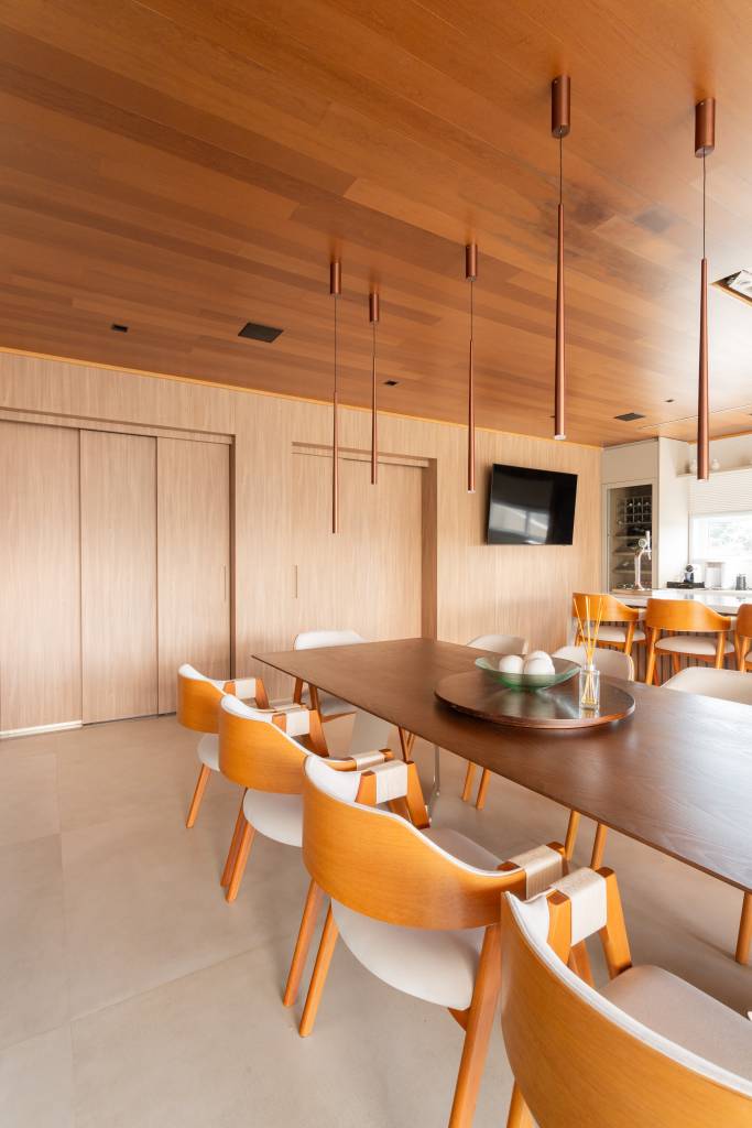 Residência de 714m² une arquitetura e paisagem em perfeita harmonia. Projeto de Casalli Arquitetura. Na foto, área social com painel de madeira.
