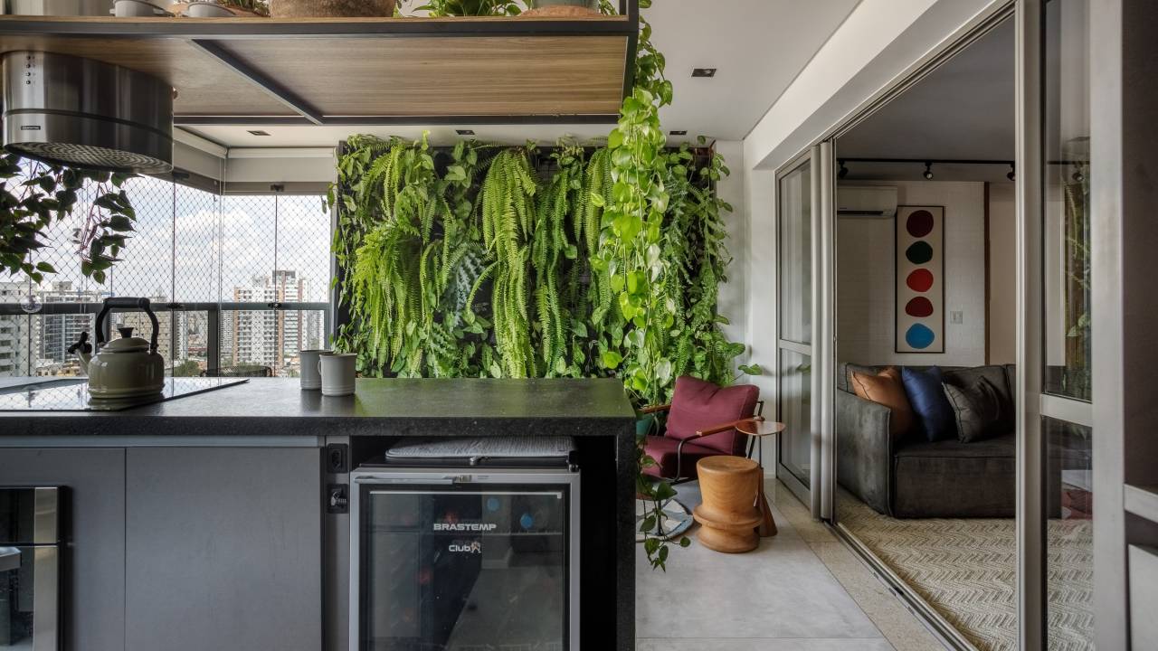 Apartamento descolado tem jardim vertical exuberante com samambaias e cozinha azul. Projeto de Flávia Campos.
