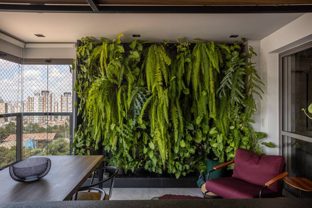 Apartamento descolado tem jardim vertical exuberante com samambaias e cozinha azul. Projeto de Flávia Campos.