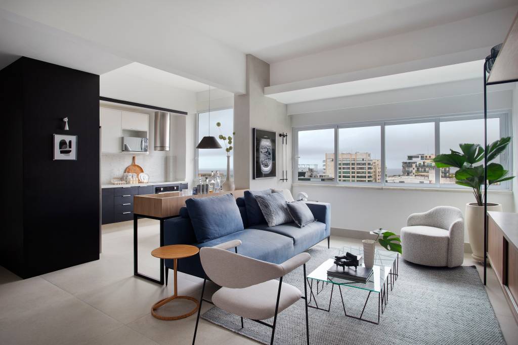 Apê tem quarto integrado à sala com porta articulada e cozinha preta e branca