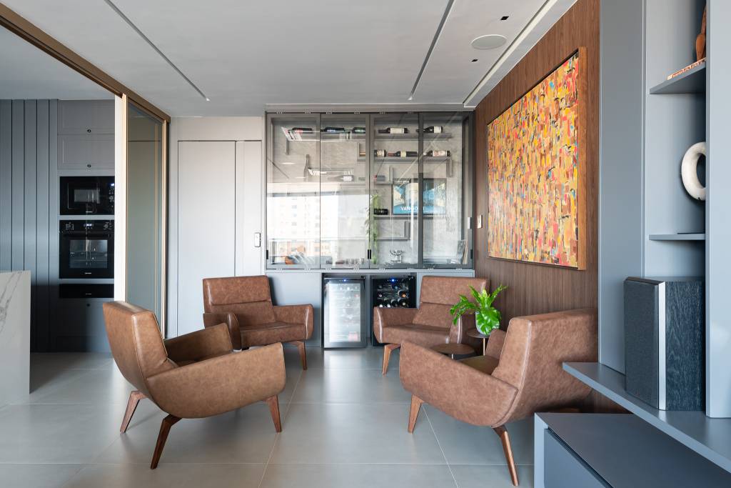 Sala de vinhos elegante tem estante personalizada, poltronas de couro e uma vitrola. Projeto de Grace Dantas Arquitetura.