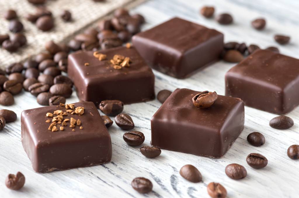 Chocolate,Sweets,With,Coffee,Beans,On,A,White,Wooden,Table. Café em receitas salgadas? Veja ideias para incorporar a bebida em pratos e sobremesas