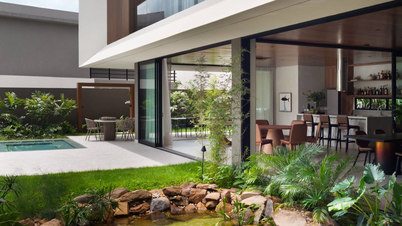 Casa elegante tem fachada com lastras de porcelanato e jardim com lago artificial. Projeto de Dois Arquitetura.