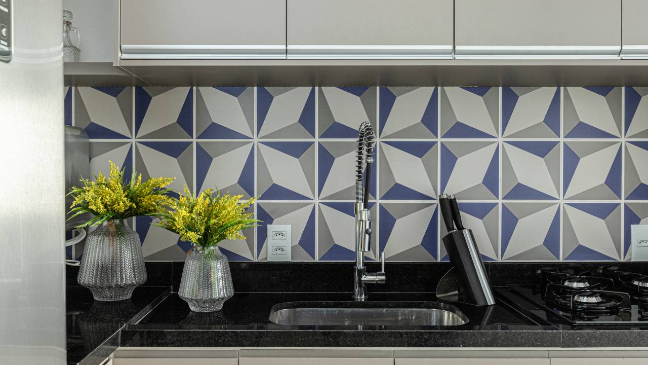 Revestimentos hexagonais em bancada dão charme extra a cozinha azul de apê. Projeto de RMV Interiores.