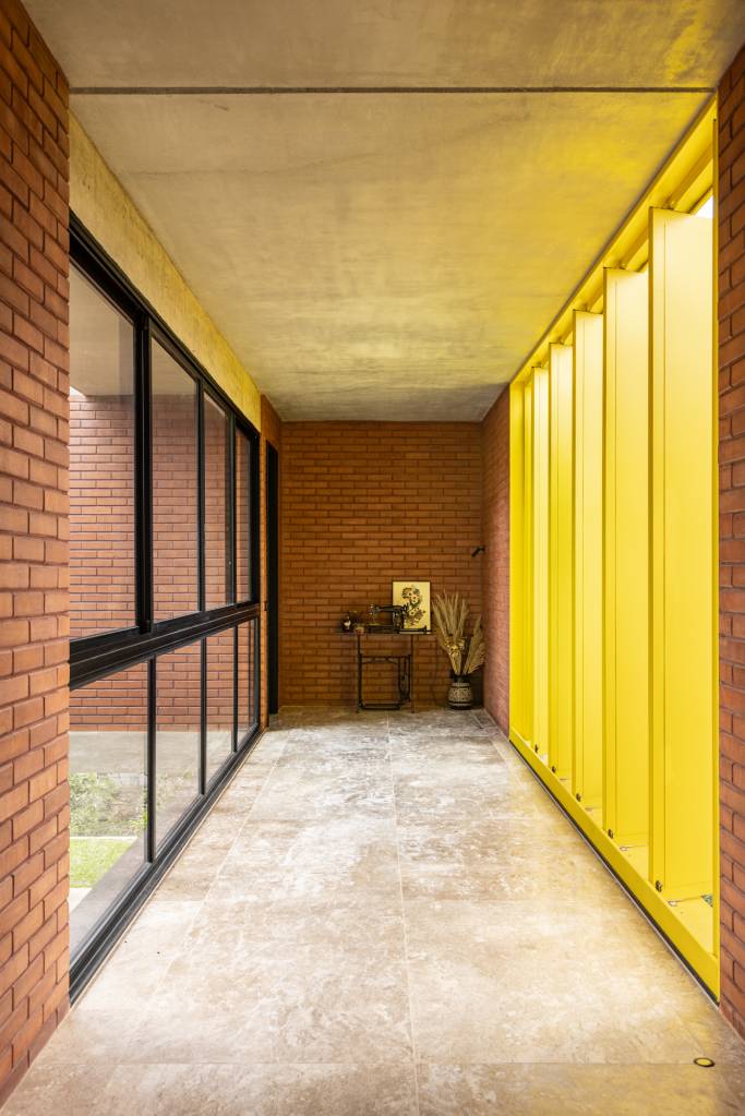 Passarela com brises metálicos amarelos conectam áreas desta casa no mato. Projeto de Hersen Mendes Arquitetura.
