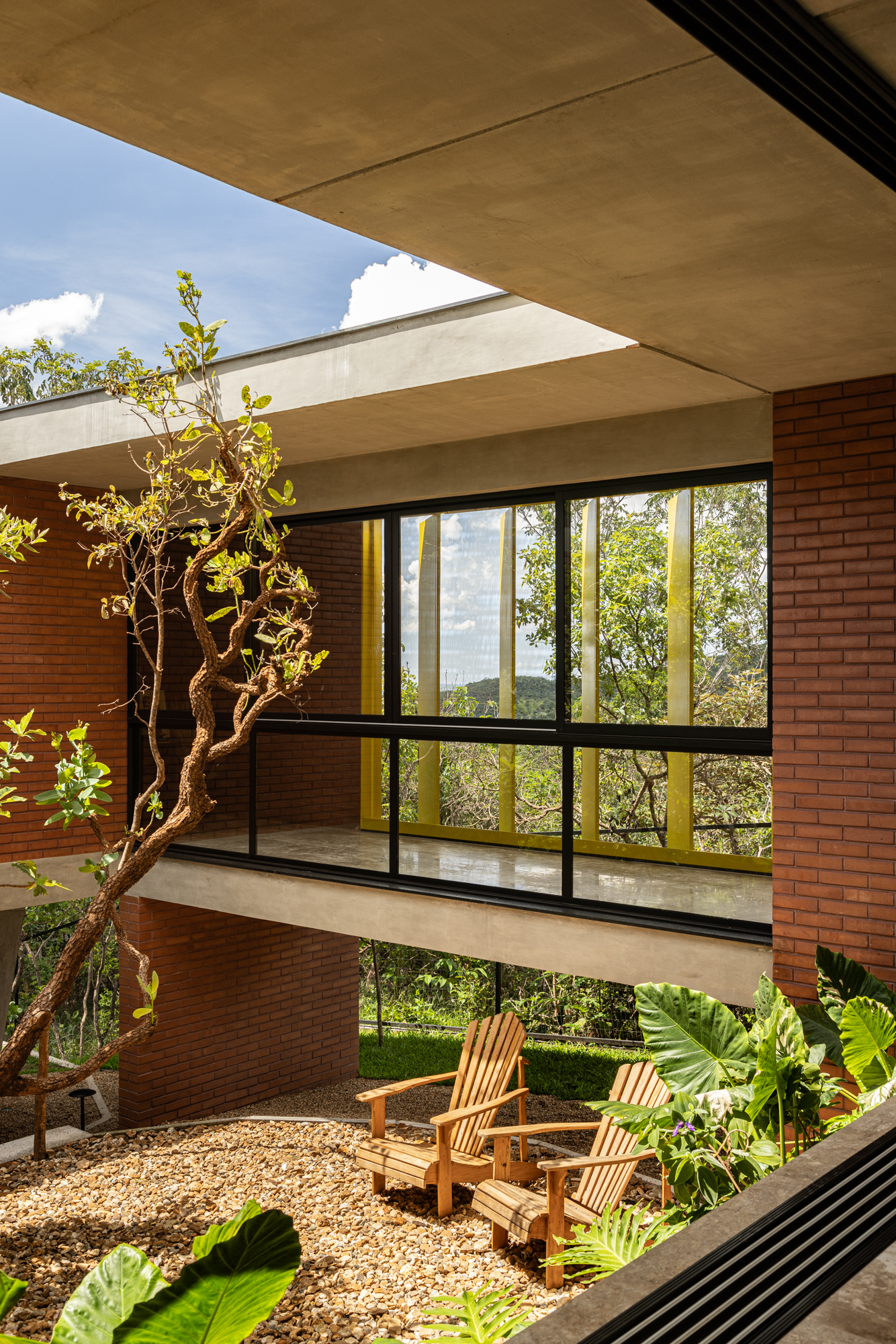 Passarela com brises metálicos amarelos conectam áreas desta casa no mato. Projeto de Hersen Mendes Arquitetura.