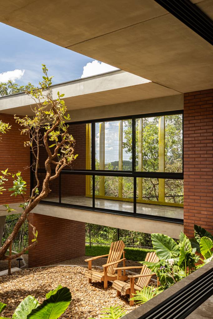 Passarela com brises metálicos amarelos conectam áreas desta casa no mato. Projeto de Hersen Mendes Arquitetura.