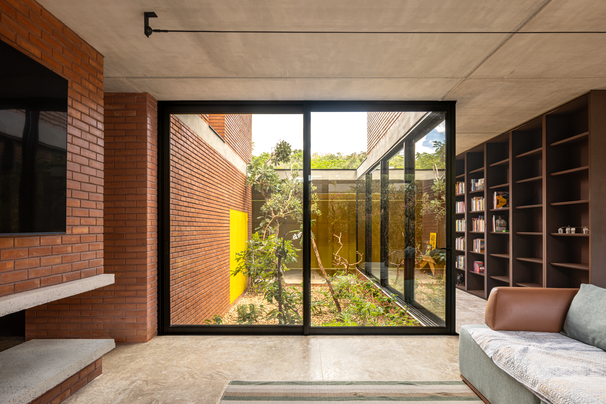 Passarela com brises metálicos amarelos conectam áreas desta casa no mato. Projeto de Hersen Mendes Arquitetura.