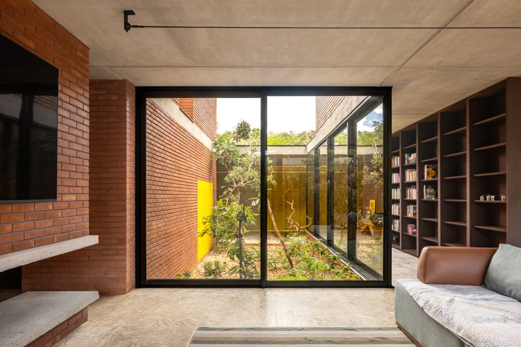 Passarela com brises metálicos amarelos conectam áreas desta casa no mato. Projeto de Hersen Mendes Arquitetura.